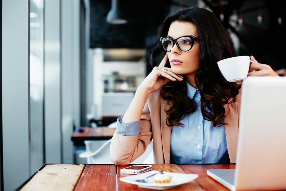 Thoughtful young woman with glasses and dark hair holding a cup of coffee
