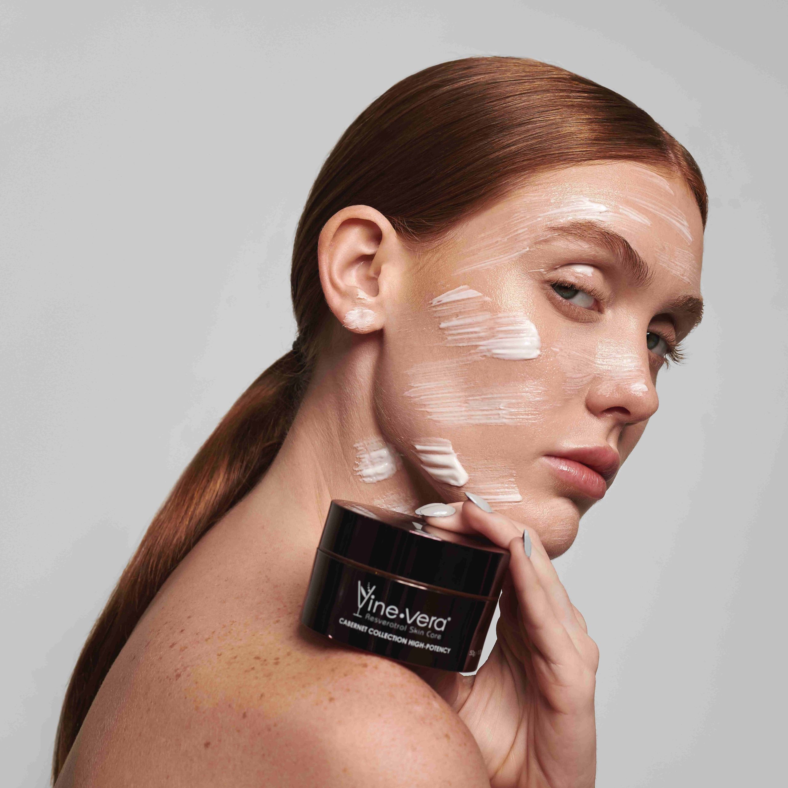 Woman with Vine Vera's resveratrol night cream on her face and wrinkles, and jar of cream in her hand
