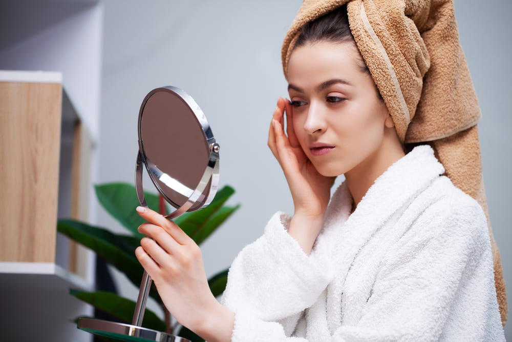Woman looking at skin in mirror at night