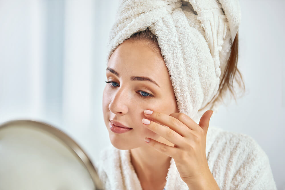 woman cleaing up skin in front of a mirror