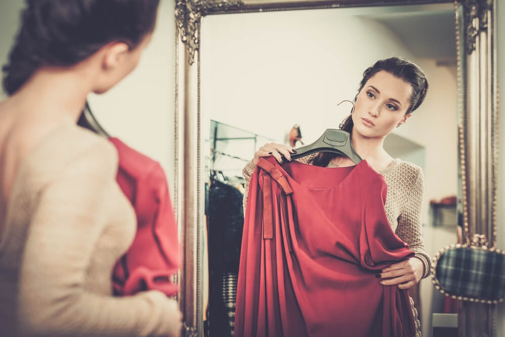 Woman trying on red dress in front of mirror