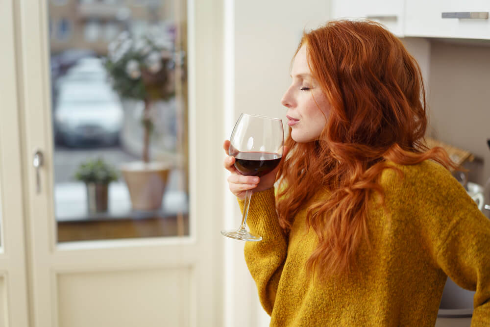 Young red-headed woman drinking red wine in the kitchen