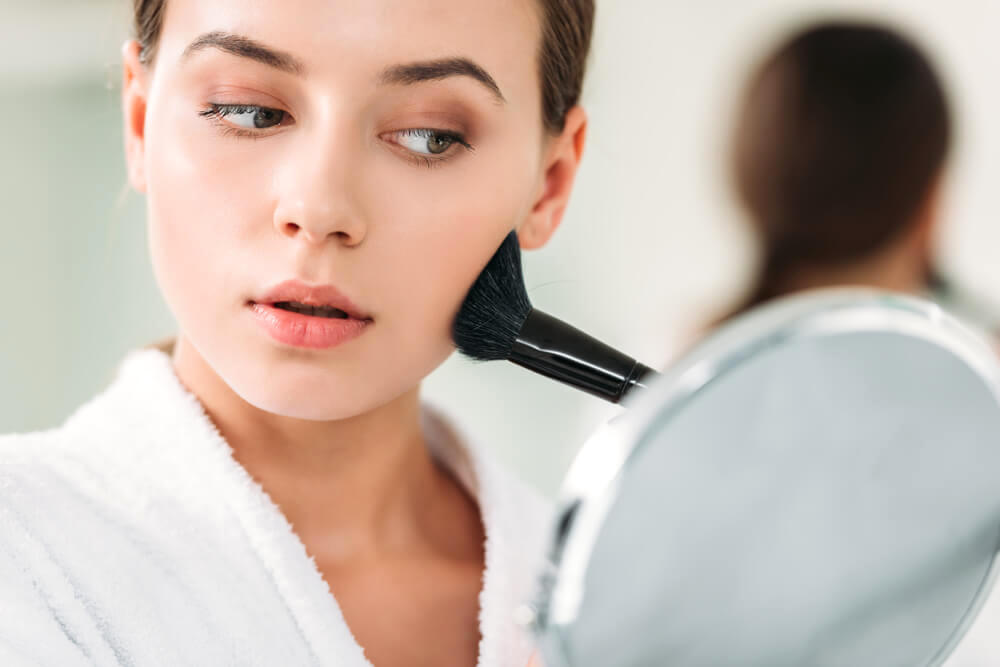 Young woman applying blush to cheeks