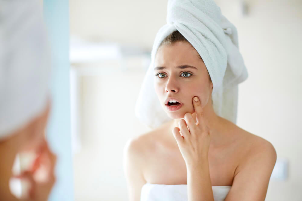 Unhappy woman pointing at pimple in the mirror