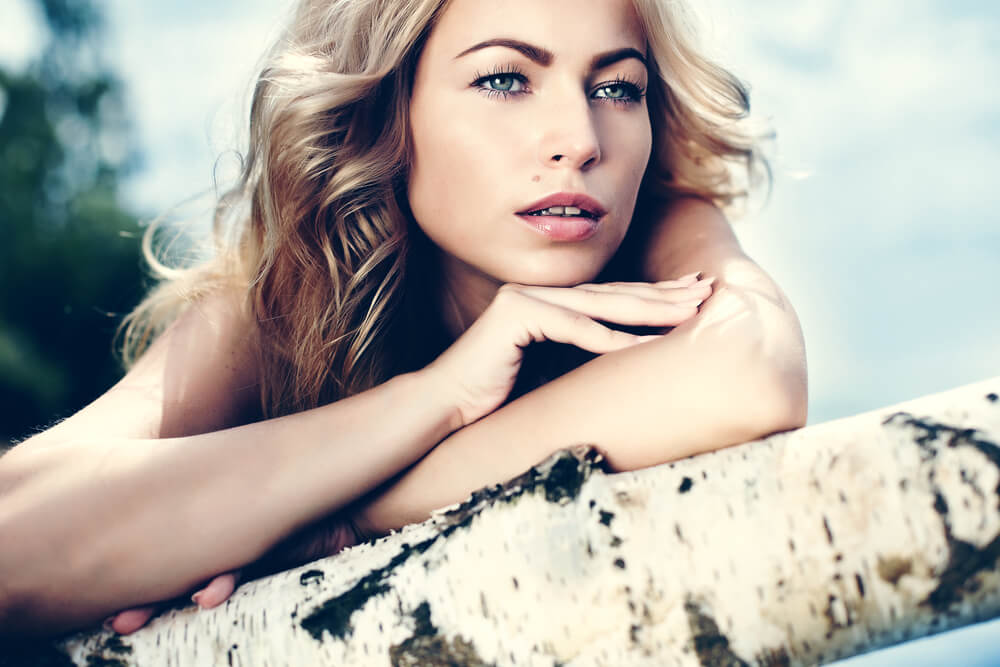Pensive young woman resting her head on a log outdoors