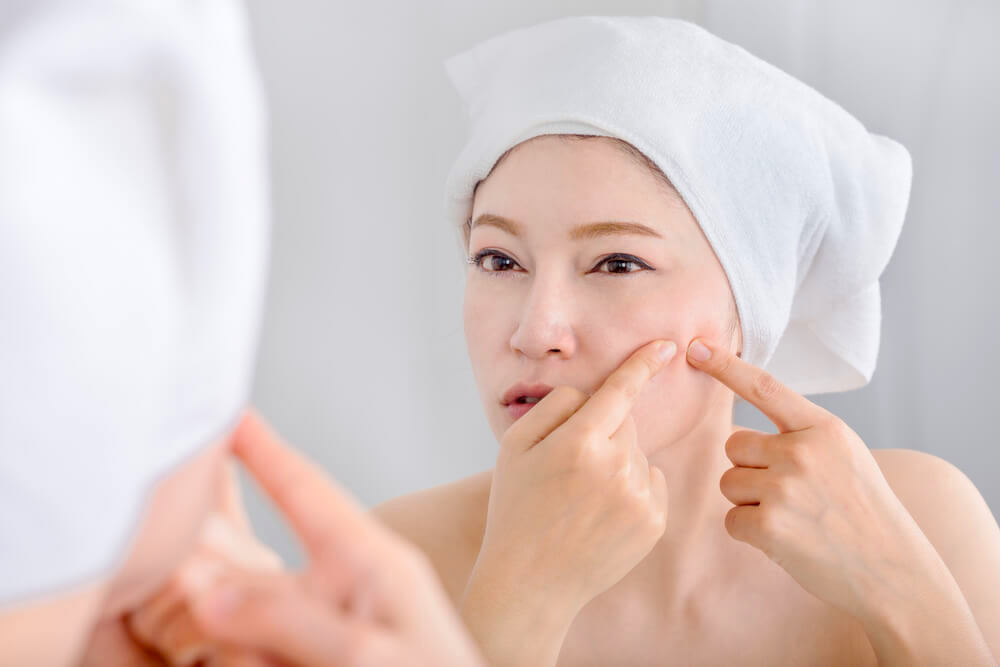woman popping pimple in front of mirror