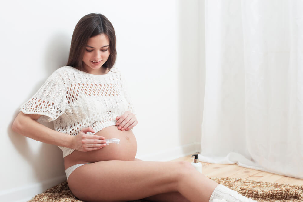 Pregnant woman applying moisturizer to belly