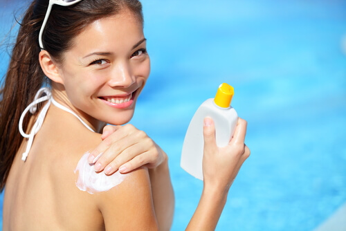 Young woman applying sunscreen to shoulder