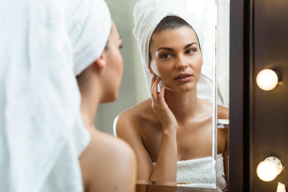 Young woman touching skin in front of bathroom mirror