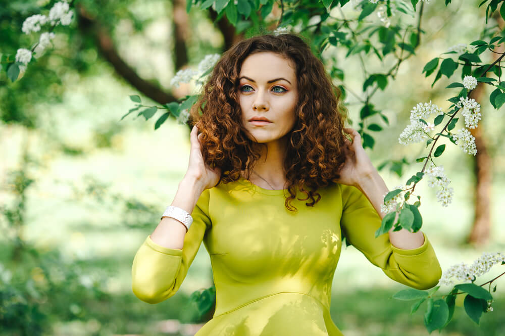 Beautiful curly-haired woman in elegant green dress in the garden