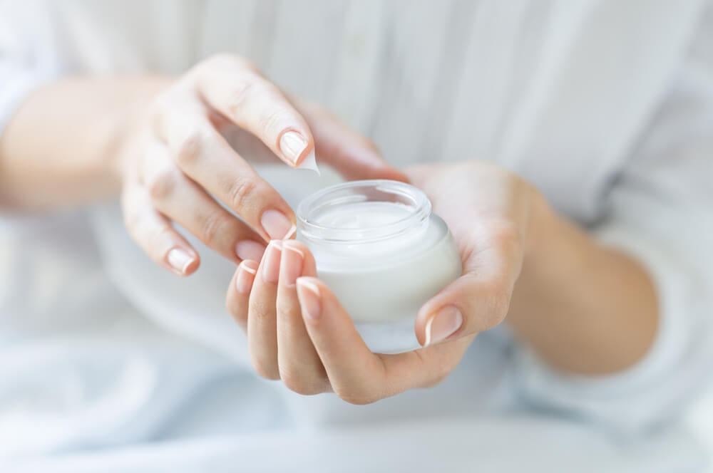 Female hands dipping into a jar of moisturizer