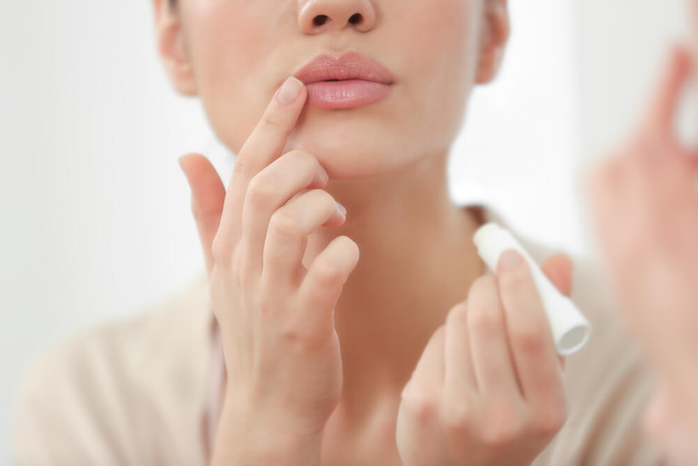 Woman applying lip balm after reading our new year's resolutions for your skin