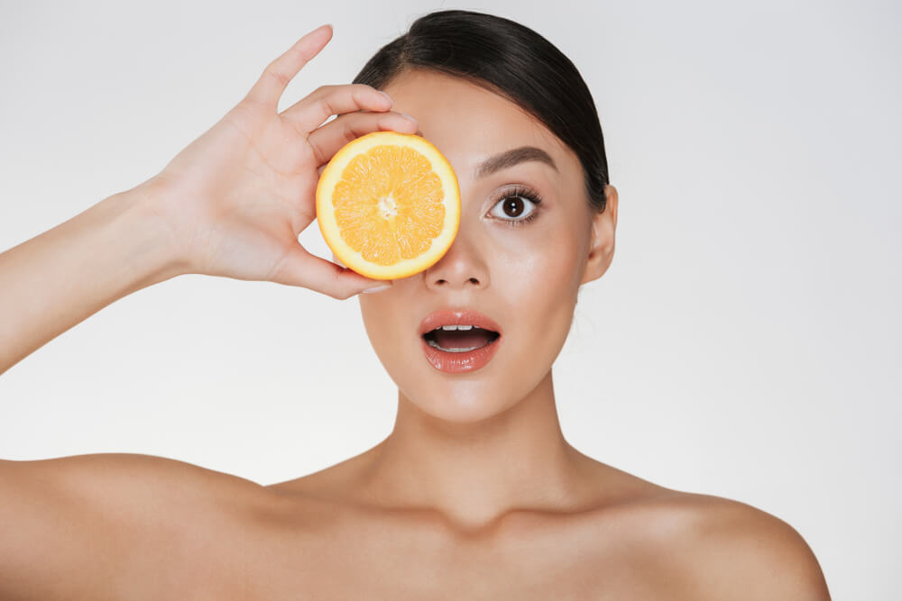 Woman with clear skin holding a slice of orange to her eye