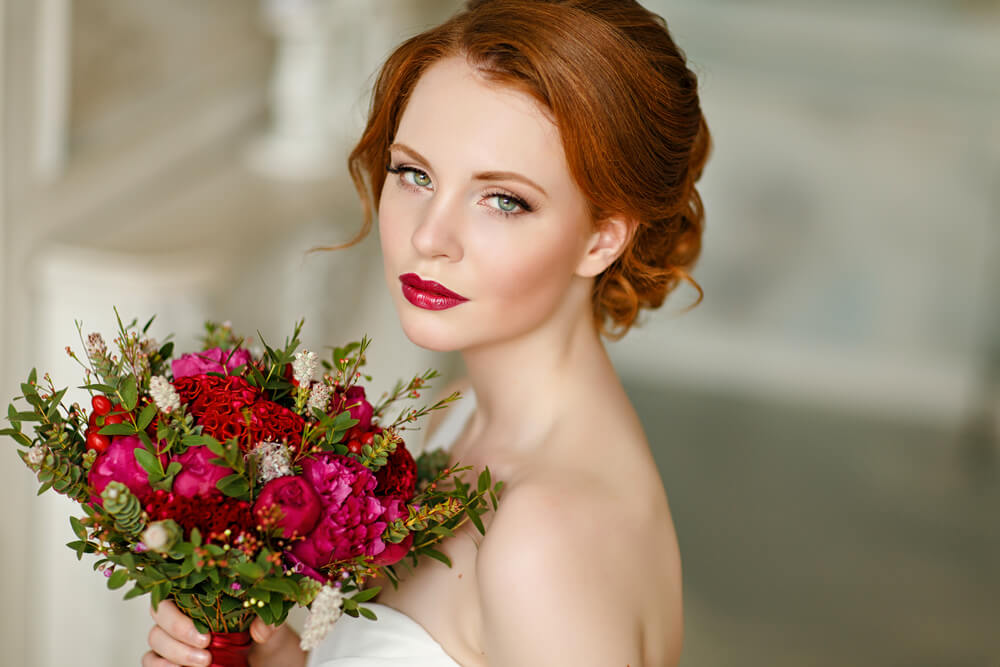 Beautiful red-headed bride with bouquet of red roses