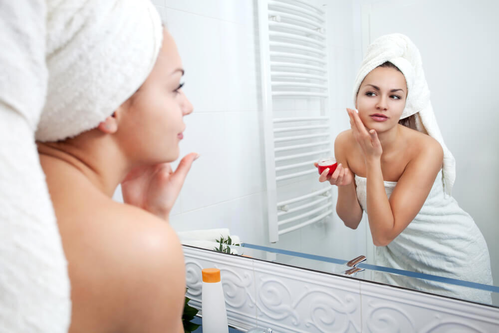 Young woman applying skincare in front of bathroom mirror