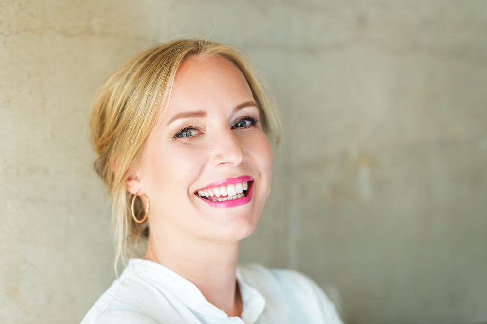 Smiling blonde woman in her 40s, in front of a pale wall
