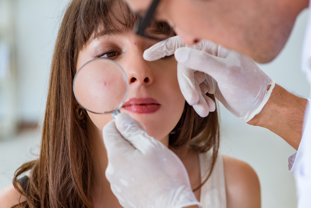 Dermatólogo examina el grano de la cara de una mujer joven