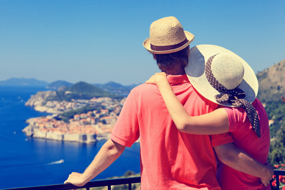 Couple wearing sunhat out on vacation together, looking out over the Mediterranean Sea