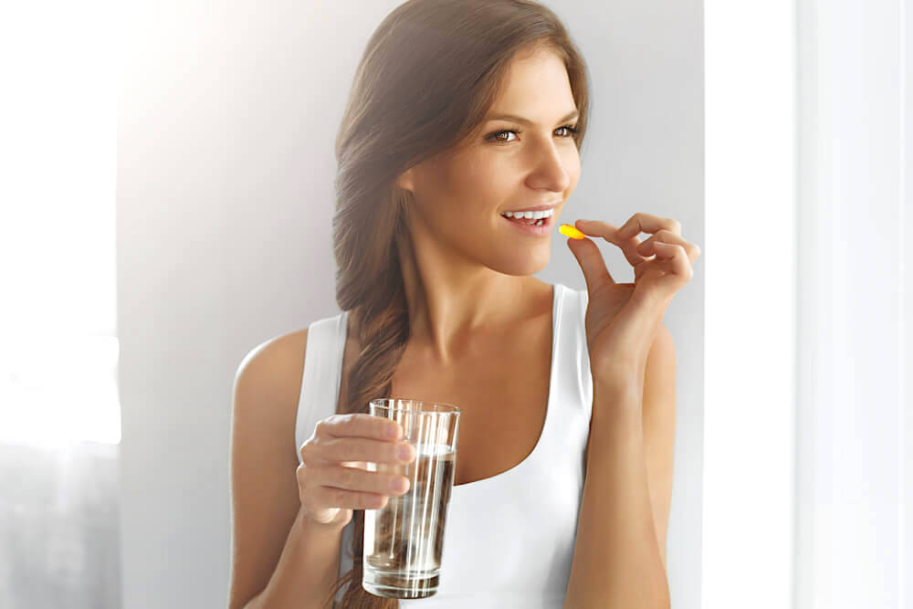 Woman taking in vitamin A pill with a glass of water
